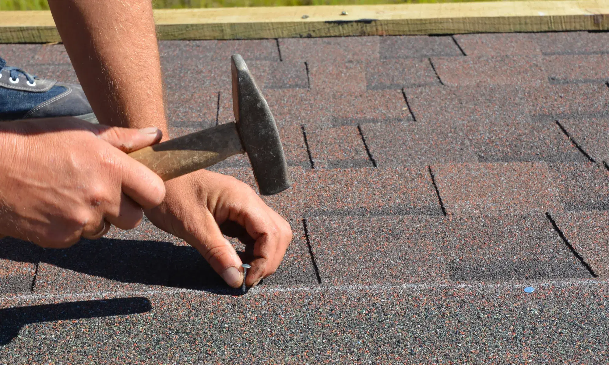 Roofer hand-nailing replacement shingles during a roof repair